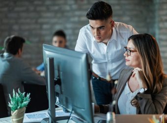 Two young business colleagues using desktop PC and reading an e-mail while working together in the office. Focus is on man.