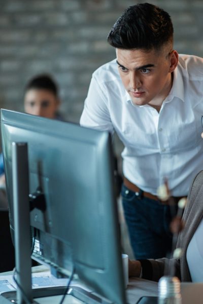 Two young business colleagues using desktop PC and reading an e-mail while working together in the office. Focus is on man.